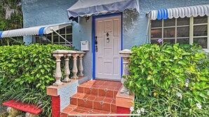 Uma casa azul com porta branca, um pequeno alpendre com um banco vermelho e um toldo azul.