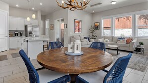 A modern kitchen with white cabinets, a stainless steel refrigerator, and a dining area with a round wooden table and blue chairs. - Flagstaff Retreat w/ Hot Tub • Firepit • Dogs OK - 1 mi to NAU (Flagstaff)