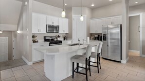 A modern kitchen with white cabinetry, stainless steel appliances, and a central island with bar stools. - Flagstaff Retreat w/ Hot Tub • Firepit • Dogs OK - 1 mi to NAU (Flagstaff)