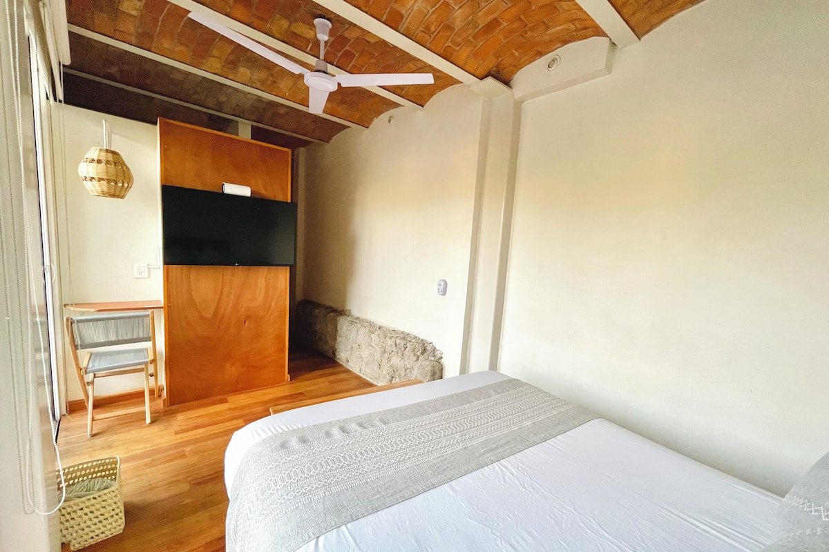 A bedroom with a bed, a wooden desk, a chair, and a ceiling fan.