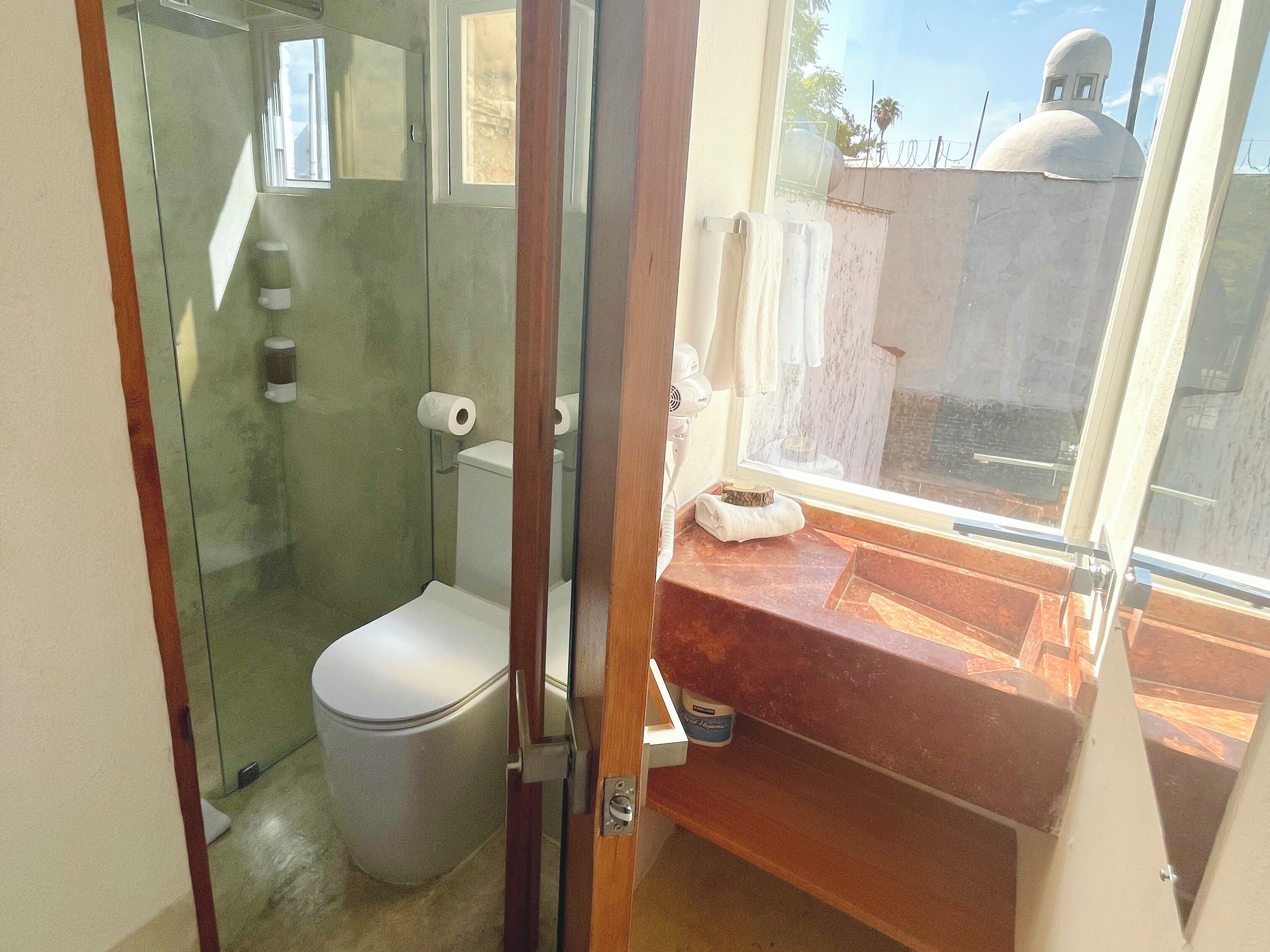 A compact bathroom with a glass shower enclosure, a toilet, and a sink with a marble countertop.