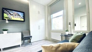 Un soggiorno moderno con un divano, una poltrona, una TV a muro e un'ampia finestra.