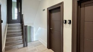 Un corridoio moderno con una scala in legno, due porte in legno scuro e una parete bianca con un piccolo cartello.