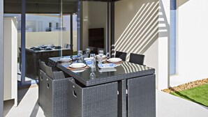 An outdoor dining area with a glass-top table, wicker chairs, and a clear view of the surrounding buildings.