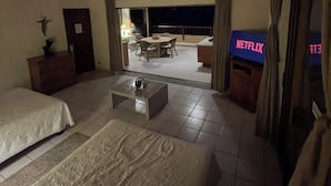 Hotellihuone, jossa on sänky, pieni pöytä, kattotuuletin ja näkymä parvekkeelle, jossa on ruokailualue.