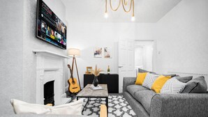 A living room with a fireplace, a television mounted on the wall, a sofa, and a coffee table. - Stylish 3 Bed House - 6 Guests - Garden - Parking (Birmingham)