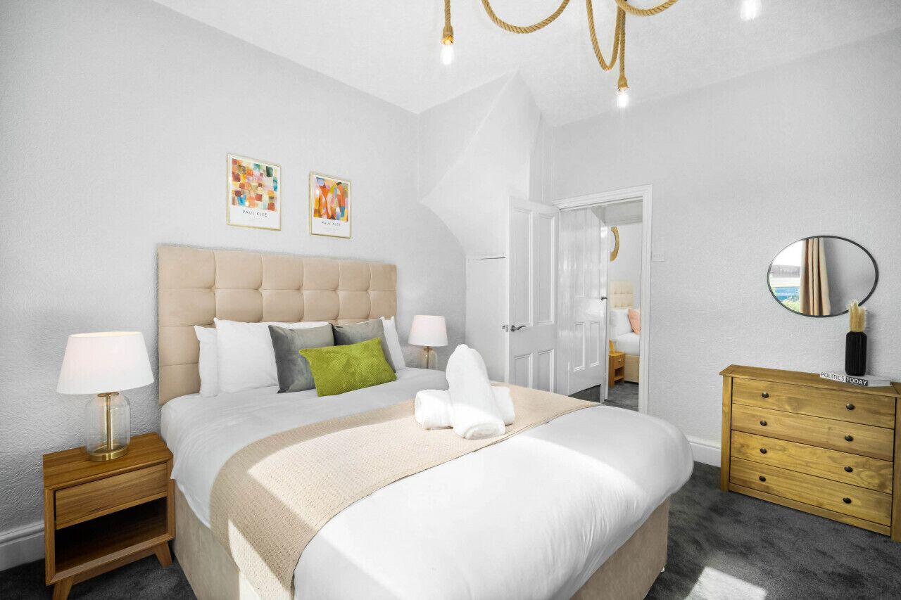 A modern bedroom with a large bed, bedside tables, a dresser, and artwork on the walls.