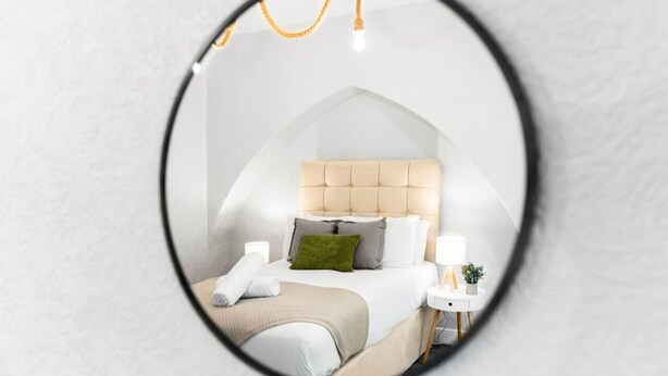 A bedroom with a tufted headboard, a bed with white linens, a green pillow, a bedside table with a lamp, and a small plant. - Stylish 3 Bed House - 6 Guests - Garden - Parking (Birmingham)