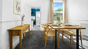 A dining area with a wooden table and chairs, a vase with flowers, and a view of the kitchen and outside. - Stylish 3 Bed House - 6 Guests - Garden - Parking (Birmingham)