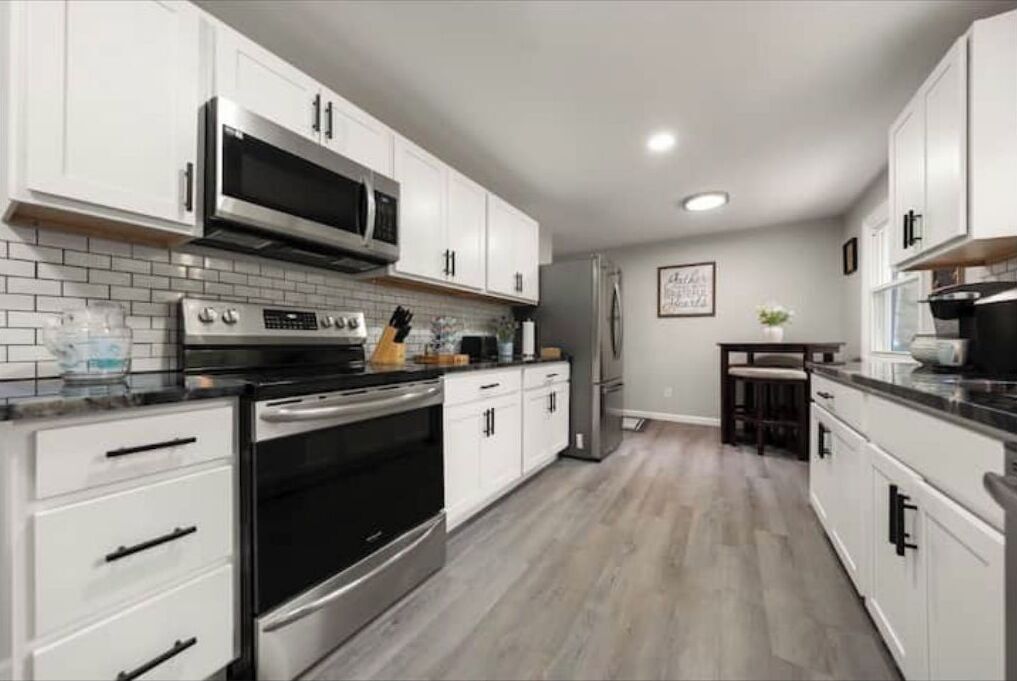 A modern kitchen with white cabinets, stainless steel appliances, and a tiled backsplash.