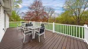 A wooden deck with a white railing, a table with chairs, and a view of trees and sky. - Fresh, fabulous home on 4 acres! (Penfield)