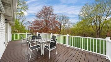 Une terrasse en bois avec une balustrade blanche, une table avec des chaises et une vue sur les arbres et le ciel.