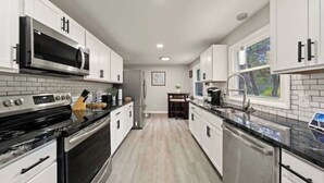 A modern kitchen with white cabinets, a black countertop, and stainless steel appliances. - Fresh, fabulous home on 4 acres! (Penfield)