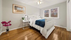 A bedroom with a white bed, a nightstand, a ceiling fan, a window with a view, and a framed picture on the wall. - Fresh, fabulous home on 4 acres! (Penfield)