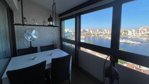 Een eethoek met een tafel en stoelen, een ventilator, en uitzicht op een haven met boten.
