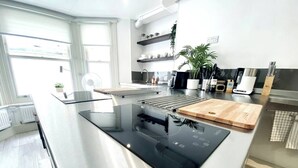 A modern kitchen with a central island, built-in appliances, and a view of the living area. - Apt. 04 -  Seaside Serenity Chic Studio Steps to Promenade (Brighton and Hove)
