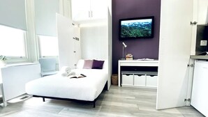 A modern bedroom with a bed, a desk, a television, and a window. - Apt. 04 -  Seaside Serenity Chic Studio Steps to Promenade (Brighton and Hove)