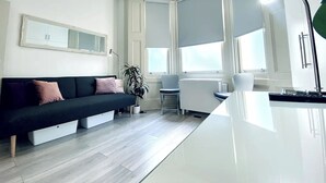 A modern living room with a dark sofa, a small table, and a potted plant. - Apt. 04 -  Seaside Serenity Chic Studio Steps to Promenade (Brighton and Hove)