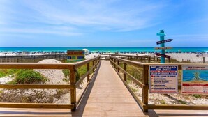 A wooden boardwalk leading to a beach with a lifeguard tower and warning signs. - Majestic Tower II - 22nd-Floor Beachfront Condo | Panoramic Gulf Views (Panama City Beach)