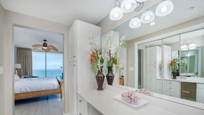 A hotel room with a bed, a large mirror, a vanity with a white countertop, and a view of the ocean. - Majestic Tower II - 22nd-Floor Beachfront Condo | Panoramic Gulf Views (Panama City Beach)