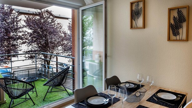 Un coin repas avec un balcon, des chaises en métal noir, une table en bois et des sets de table à motifs noir et blanc.