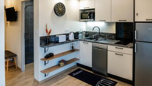 Une cuisine moderne avec des armoires blanches, un comptoir noir, un four à micro-ondes, un réfrigérateur et une horloge murale.