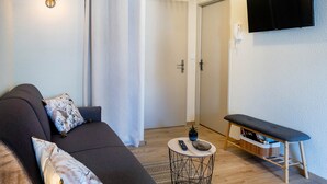 Un salon comprenant un canapé, une table basse ronde, un banc et un téléviseur fixé au mur.