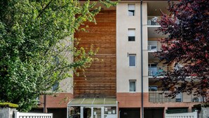 Un immeuble résidentiel à plusieurs étages, doté d’une façade moderne, d’une entrée abritée et d’un espace de stationnement sécurisé par une grille.
