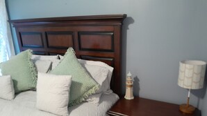A neatly made bed with a wooden headboard, a bedside lamp, and a nightstand with drawers.