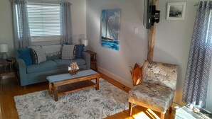 A living room with a sofa, a coffee table, a patterned armchair, a painting, and a television.