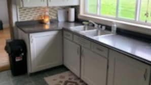 A kitchen with white cabinets, a sink, and a window with blinds.