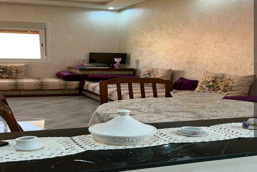 A cozy living room with a sofa set, a dining table with a decorative centerpiece, and a television on a stand.