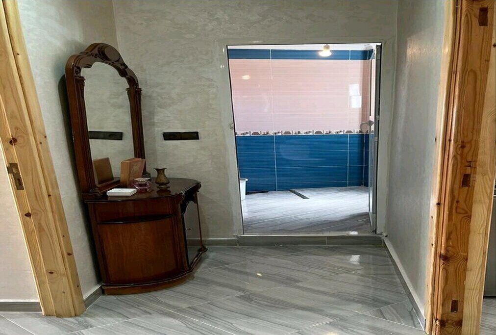 A bathroom with a wooden vanity, a large mirror, and a blue tiled shower area.