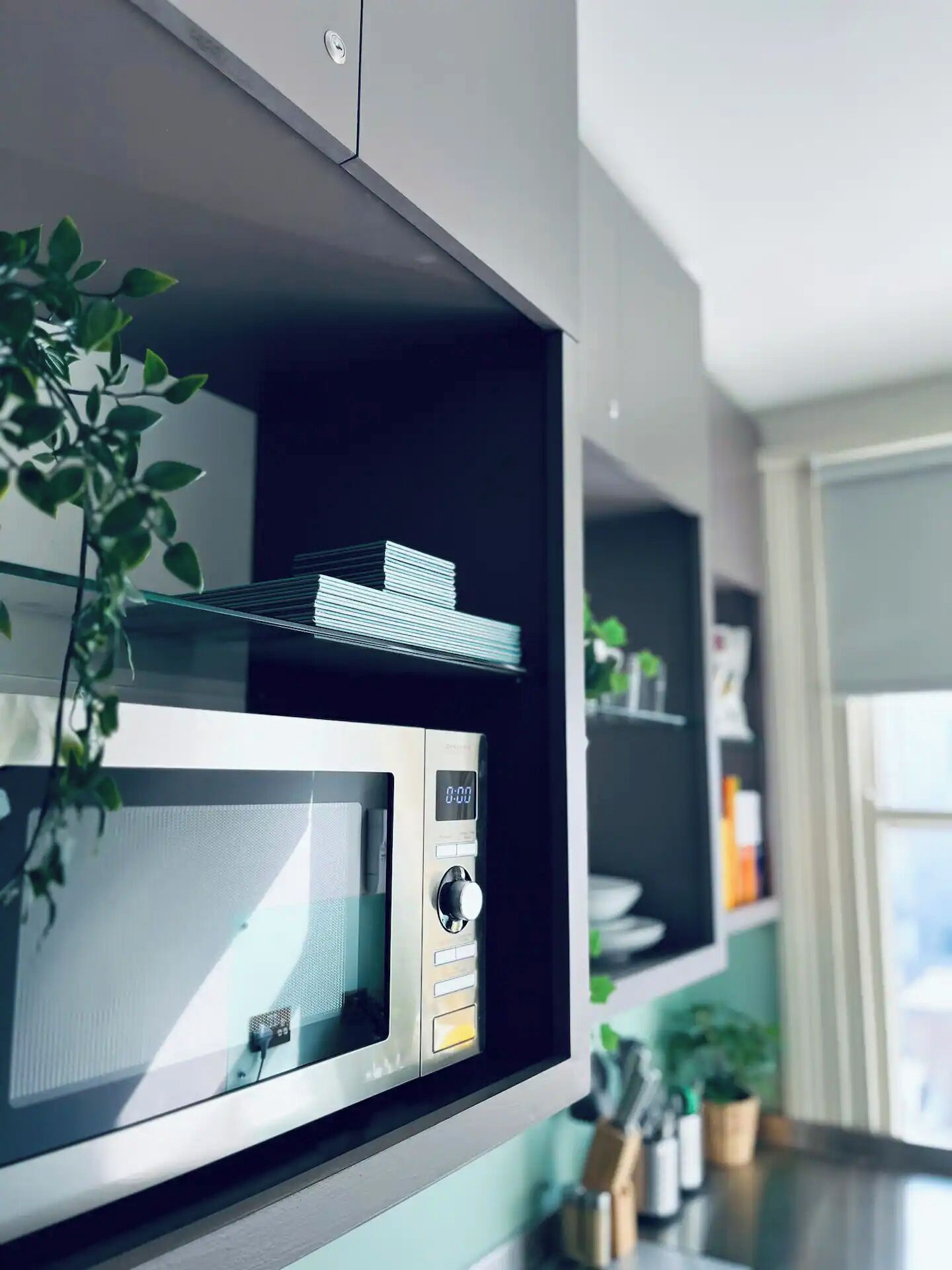 A kitchen with a built-in microwave, a digital clock, and a plant on the counter.