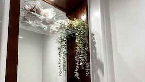 A bathroom with a wooden vanity, a glass shelf with toiletries, and hanging plants. - Apt. 05 - Stylish Studio Steps from Sea, Bars & Promenade (Brighton and Hove)