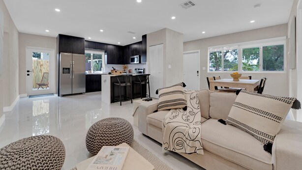 A modern living room with a sofa, ottoman, and a dining area with a table and chairs.