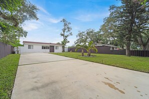 Stroll through the well-manicured yard, surrounded by trees and a wooden fence, to the single-story house with a flat roof and garage door.