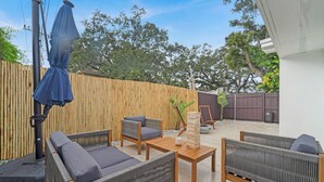 An outdoor patio with wicker furniture, a wooden table, and a blue umbrella.