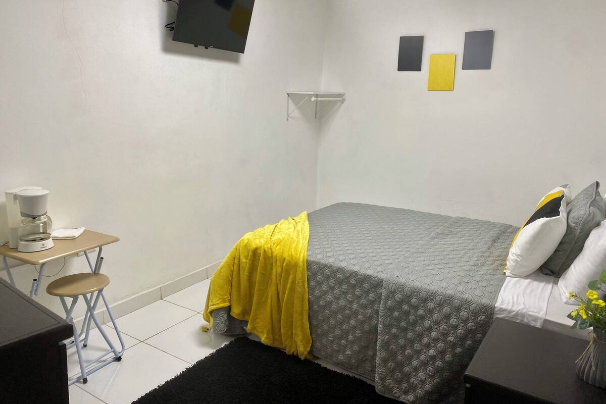 Une petite chambre à coucher, bien rangée, avec un lit, une table de chevet et un téléviseur fixé au mur.