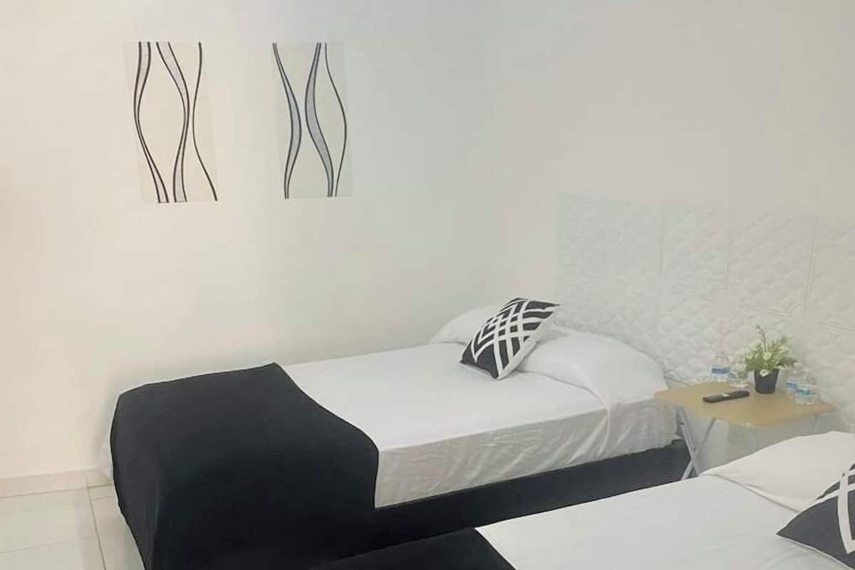 Une chambre d’hôtel avec deux lits, chacun agrémenté de draps noirs et blancs, une petite table de chevet avec une plante et des œuvres d’art abstraites accrochées au mur.