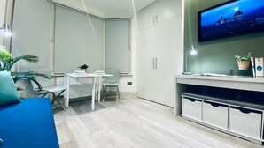 Een moderne, goed verlichte kamer met een eettafel, stoelen, een aan de muur bevestigde televisie en een potplant.