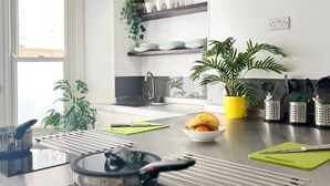 Een moderne keuken met een ingebouwd fornuis, een spoelbak en een raam. Er staan planten op het aanrecht en een plank met servies.