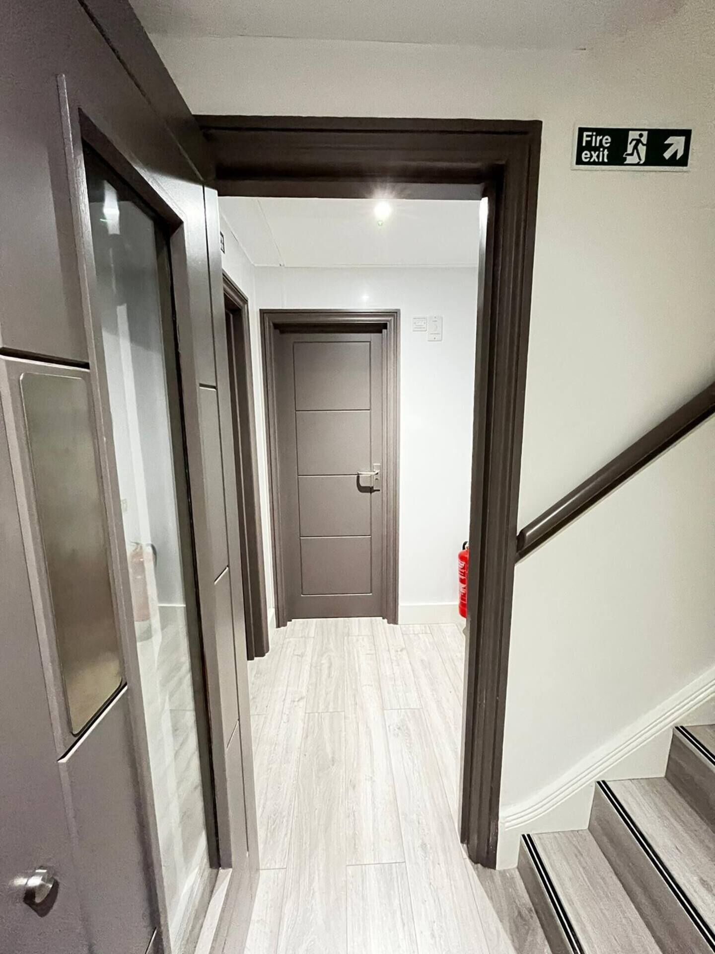 Un pasillo con letrero de salida de emergencia, una puerta y un extintor.