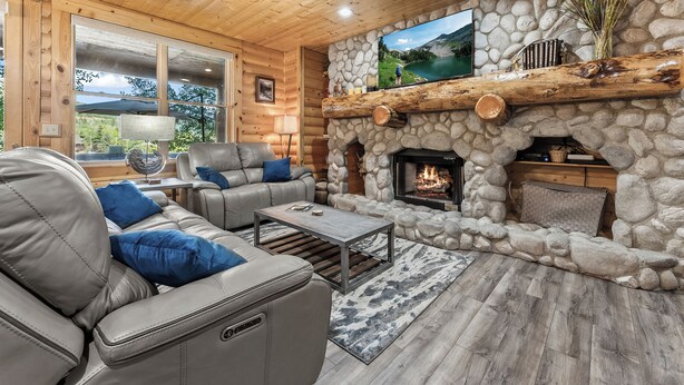 L’intérieur chaleureux d’un chalet avec une cheminée en pierre, des canapés en cuir et une grande fenêtre donnant sur un paysage magnifique.