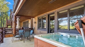 Une terrasse en bois avec un jacuzzi, des sièges d’extérieur et de grandes fenêtres donnant sur un paysage pittoresque.