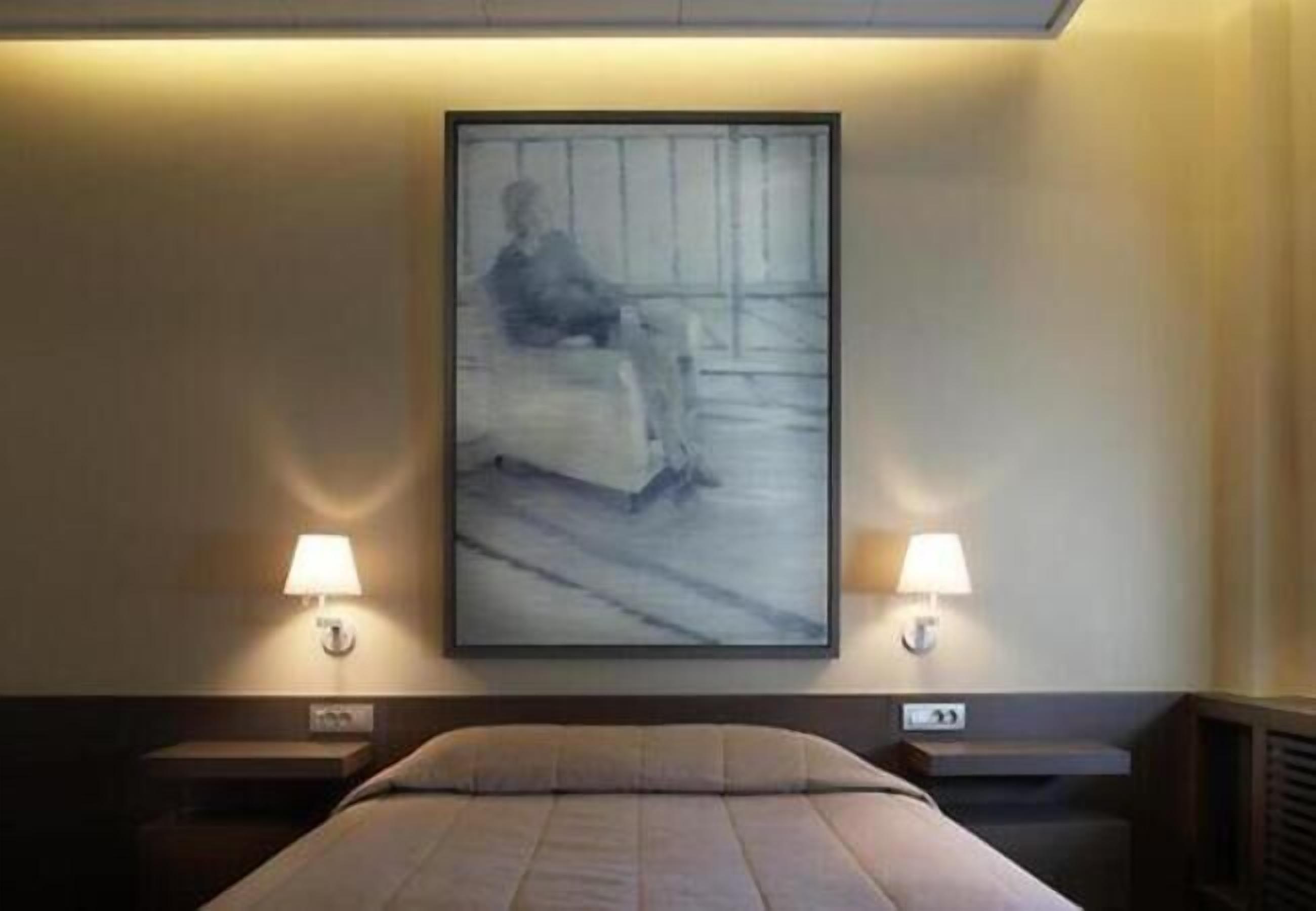 Ein Hotelzimmer mit einem Bett, zwei Nachttischlampen und einem gerahmten Kunstwerk an der Wand.