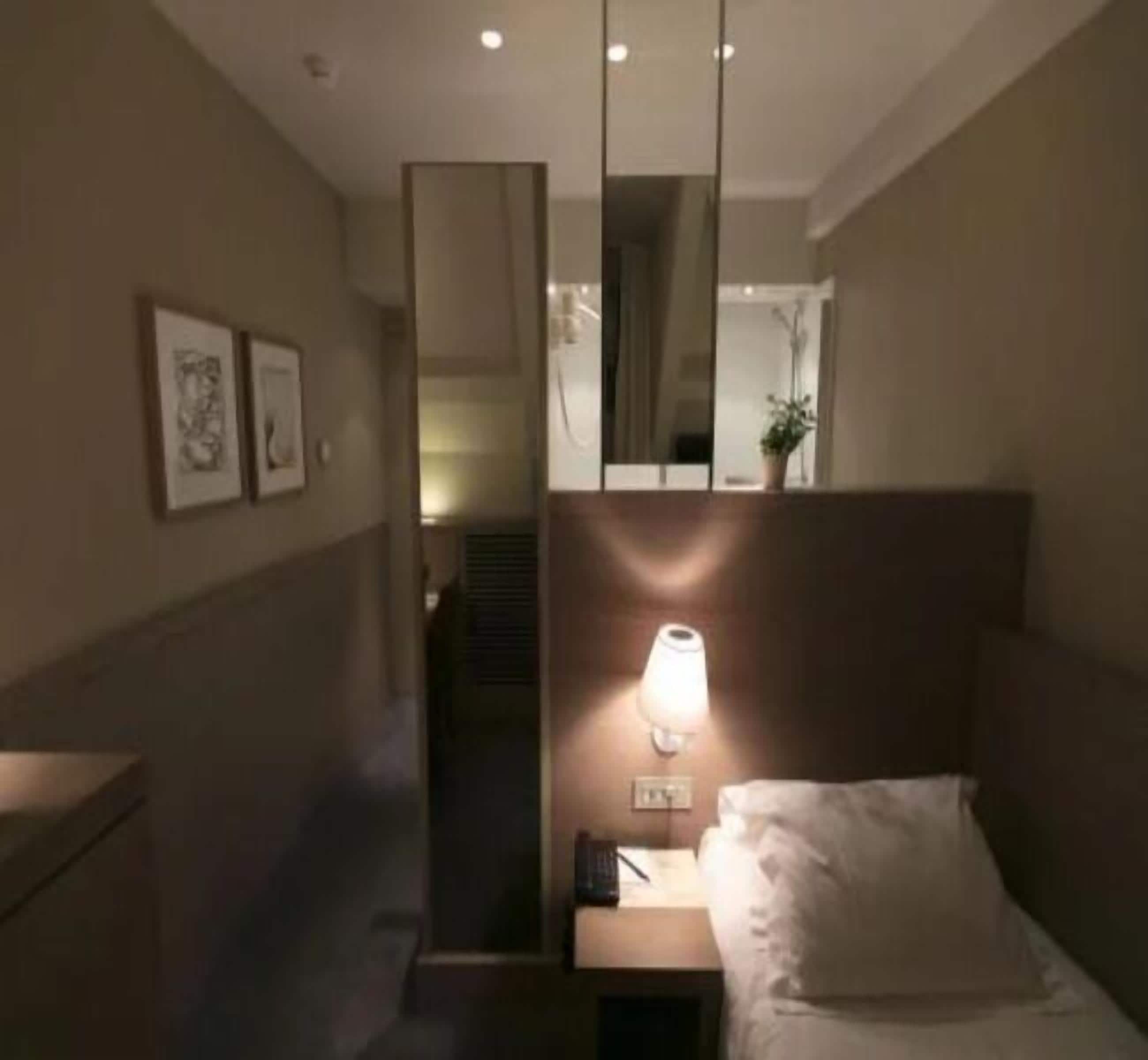 Una habitación de hotel con cama, mesita de noche, lámpara y una obra de arte en la pared.