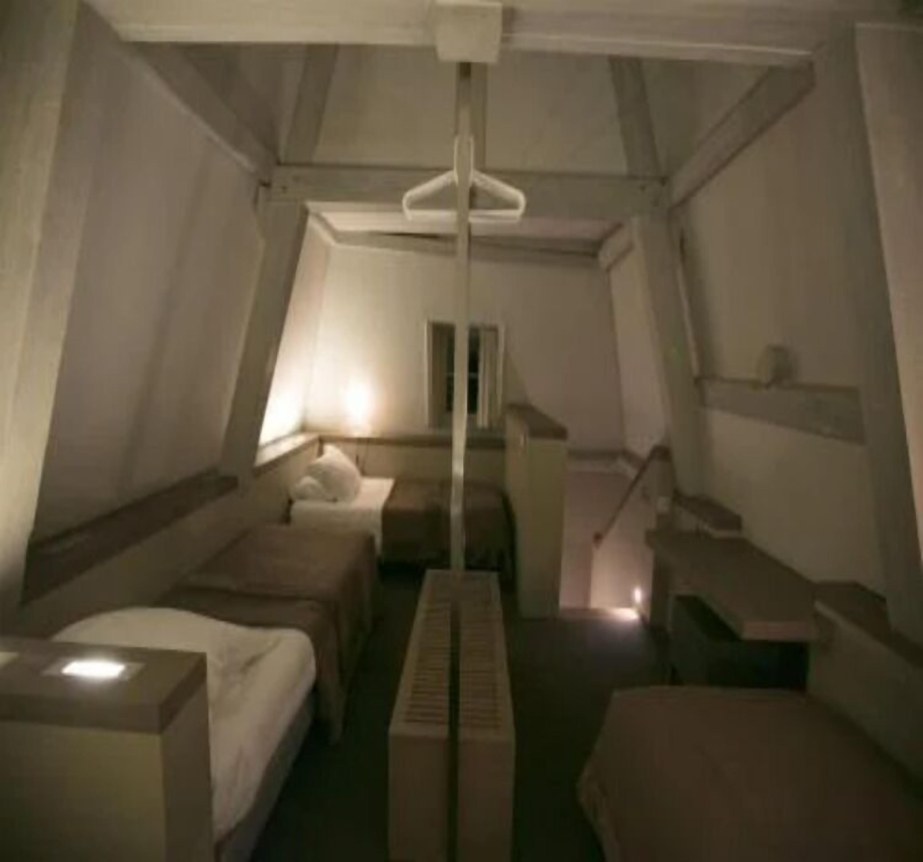 Une pièce avec un plafond en pente, deux lits, une petite table et une fenêtre.