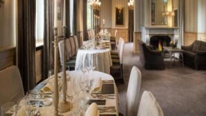 Une salle à manger élégante, avec de longues tables dressées pour le repas, une cheminée et un coin salon confortable.