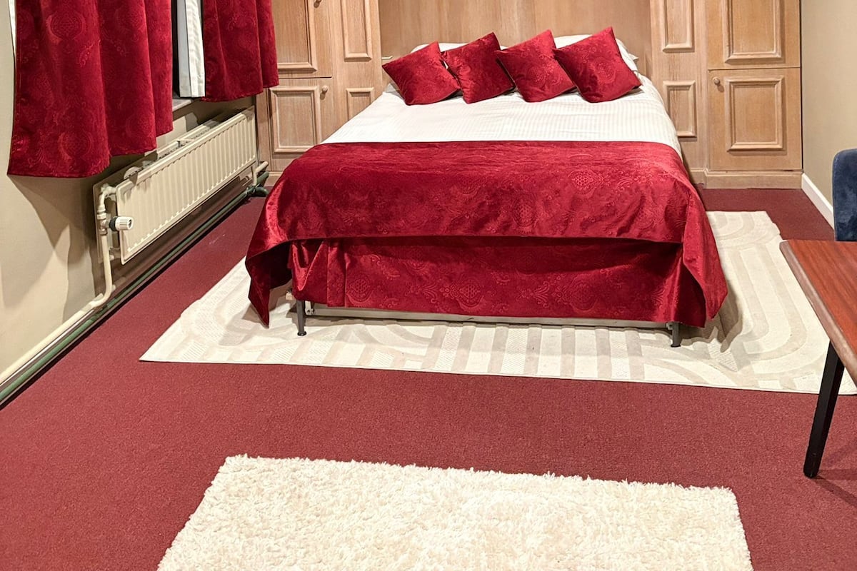 A bedroom with a large bed, red curtains, a wooden wardrobe, and a radiator.
